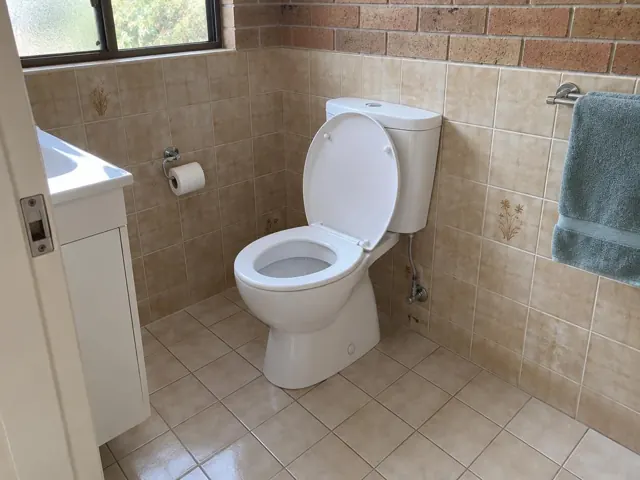 Clean white toilet in a tiled bathroom with tan walls and tiled floor in Seven Hills