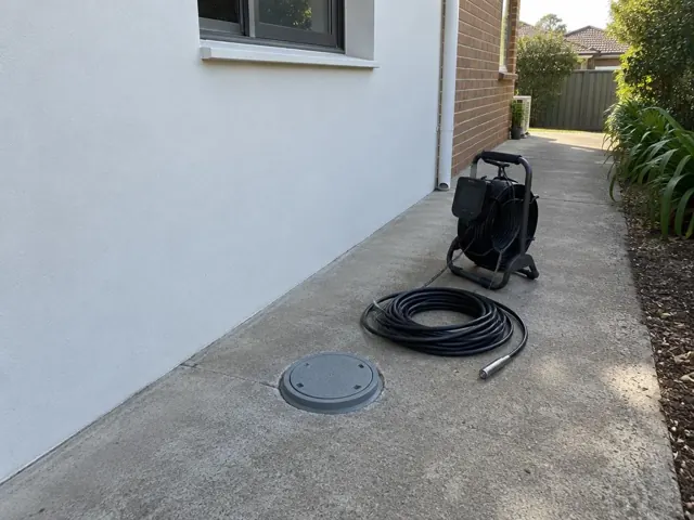 Capped inspection opening beside a drain camera reel on a concrete side path by a brick house in Doonside