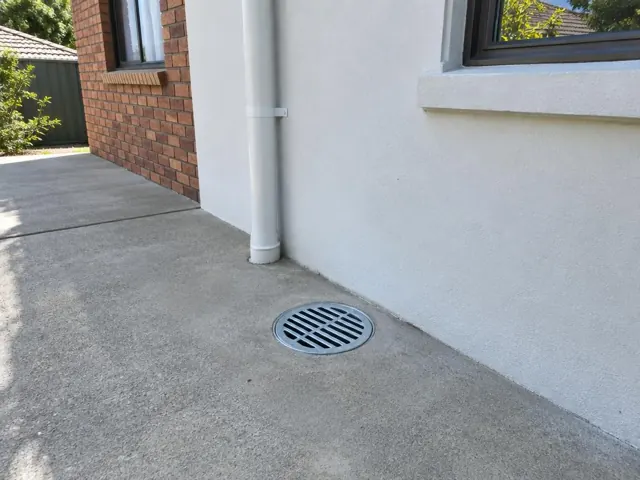 Outdoor gully grate on a concrete slab beside a white wall and brick house in Blacktown