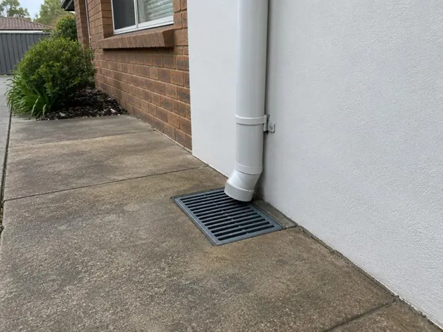 Concrete side path with a grated stormwater drain beside a house wall and downpipe in Blacktown